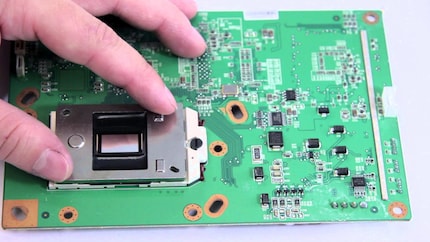 Der DMD-Chip ist das ca. 1 × 1,5 cm grosse, silberne Plättchen zwischen Daumen und Zeigefinger.