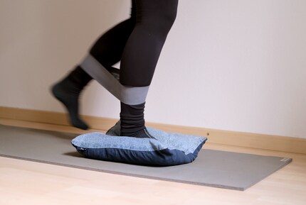 While one leg is on the cushion, the other is moved in a semi-circle from front to back against the resistance of the fitness band.