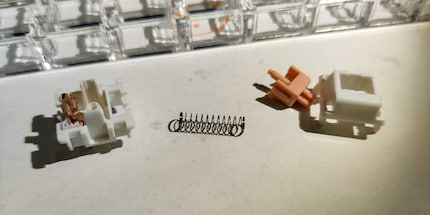 Die Einzelteile eines unmoralischen Pandas: Gehäuseunterteil mit Mechanik, Feder, Stengel und Gehäuseoberteil (von links nach rechts).