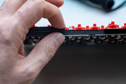 Zwischen Deckplatte und Platine siehst du die Dämmmatte. Was ich da mit den Fingern zusammendrücke, sind die Gaskets, die der Tastatur ihr flexibles Tippgefühl geben.