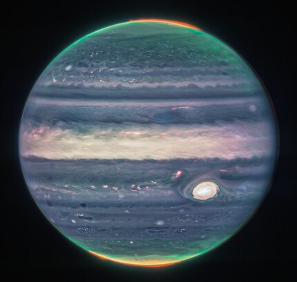 Die Polarlichter sind auf dieser Version des Bildes rot eingefärbt. Der weisse Fleck ist der grösste Wirbelsturm des Sonnensystems.
